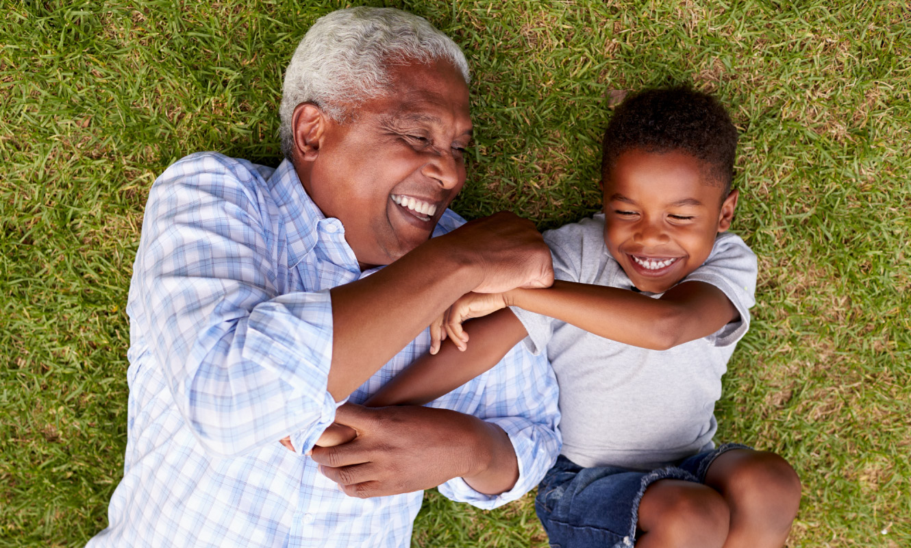 Grandfather and grandson tickle each other and laugh as they lay on the green grass