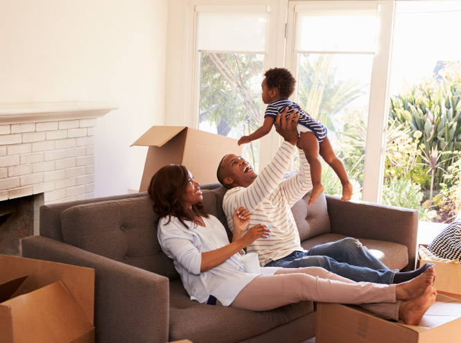 Family of three sitting on their couch in new home with moving boxes around them
